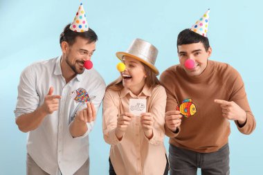 Business colleagues with clown noses and paper fishes on blue background. April Fools' Day celebration