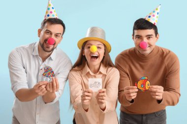Business colleagues with clown noses and paper fishes on blue background. April Fools' Day celebration