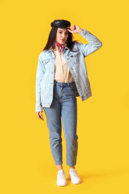 Stylish young woman in cap on yellow background