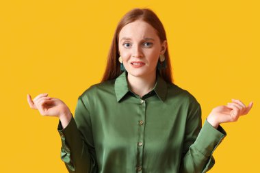 Confused young redhead woman on yellow background