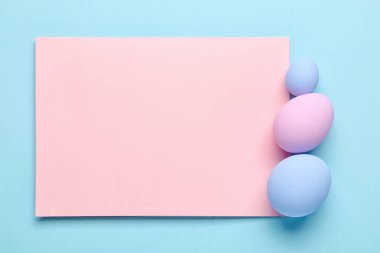 Blank card and painted Easter eggs on color background