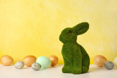 Easter bunny and painted eggs on table against yellow background