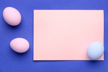 Blank greeting card and painted Easter eggs on blue background