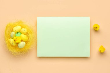 Blank greeting card, nest with Easter eggs and baby chickens on beige background