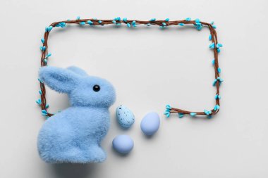 Frame made of vine, painted eggs and Easter bunny on beige background