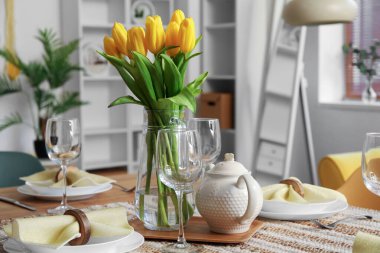 Table setting for International Women's Day celebration with tulip flowers and teapot in interior of room
