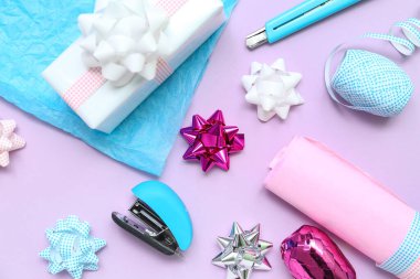 Bows made of ribbons with gift box, wrapping paper and stapler on lilac background