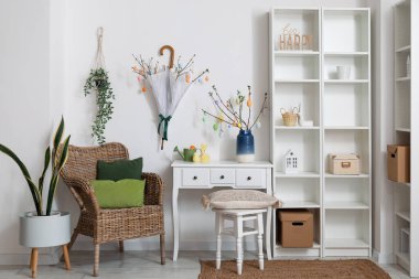 Interior of light living room with Easter decor, armchair and shelving unit