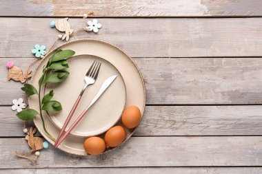 Table setting with Easter eggs, cutlery and plant branch on grey wooden background