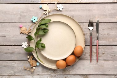 Table setting with Easter eggs, cutlery and plant branch on grey wooden background
