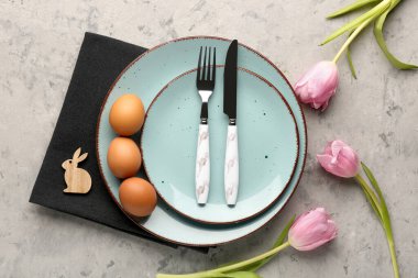 Table setting with Easter eggs, cutlery and tulip flowers on grey grunge background