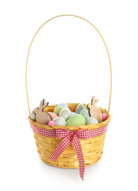 Basket with painted Easter eggs and wooden bunny figures on white background