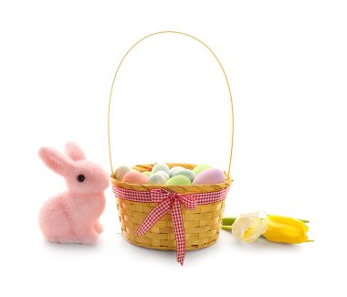 Basket with Easter eggs, tulip flowers and toy bunny on white background