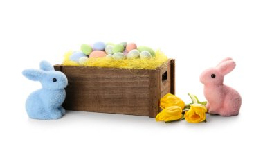 Box with painted Easter eggs, tulip flowers and toy bunnies on white background
