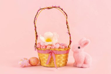 Basket with beautiful Easter eggs, flower and toy bunny on pink background