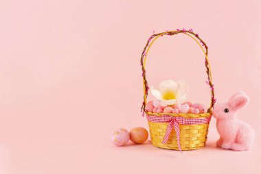 Basket with beautiful Easter eggs, flower and toy bunny on pink background
