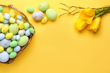 Basket with painted Easter eggs and bouquet of tulip flowers on yellow background