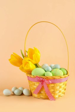 Basket with beautiful Easter eggs and tulip flowers on color background