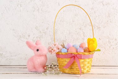 Basket with beautiful Easter eggs, flowers and toy bunny on light wooden table