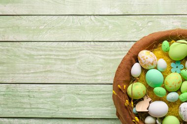 Basket with beautiful Easter eggs and decor on color wooden background