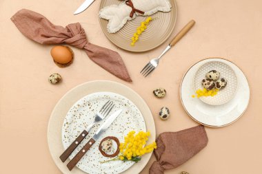 Stylish table setting with Easter eggs and mimosa flowers on color background