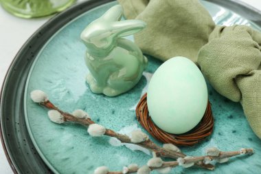 Stylish table setting with Easter egg, willow branches and ceramic bunny, closeup