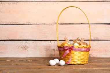 Wicker basket with painted Easter eggs on wooden table near beige wall