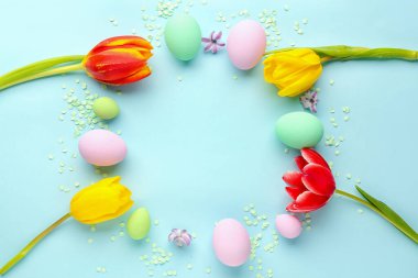 Frame made of Easter eggs, spring flowers and confetti on color background
