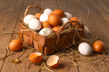 Wicker basket with Easter eggs and hay on brown wooden background