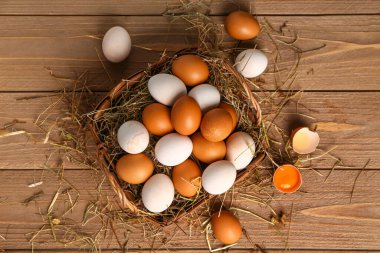 Wicker basket with Easter eggs and hay on brown wooden background
