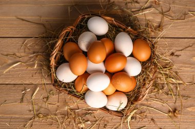 Wicker basket with Easter eggs and hay on brown wooden background