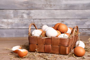 Wicker basket with Easter eggs and hay on wooden table near grey wall