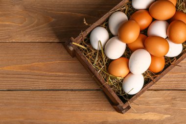 Wicker basket with Easter eggs and hay on brown wooden background