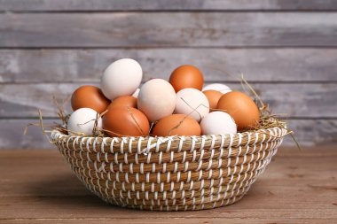 Wicker basket with Easter eggs and hay on wooden table near grey wall