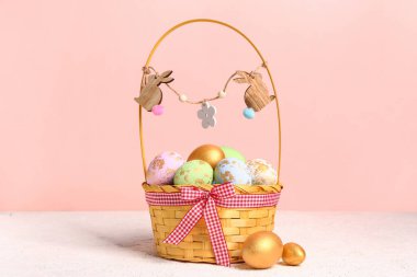 Wicker basket with painted Easter eggs on white table near pink wall
