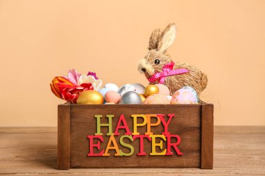 Easter eggs, bunny and tulip flowers in basket with text HAPPY EASTER on wooden table near beige wall