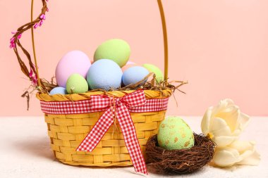 Wicker basket with painted Easter eggs and tulip flowers on white table near pink wall