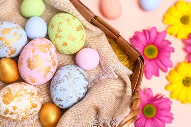 Wicker basket with painted Easter eggs and chrysanthemum flowers on pink background