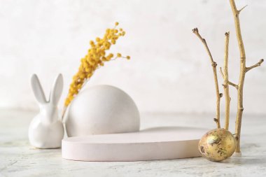 Composition with podiums, tree branches, Easter egg, bunny and mimosa flowers on light background