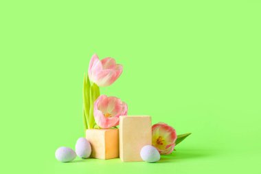 Composition with podiums, tulip flowers and Easter eggs on green background