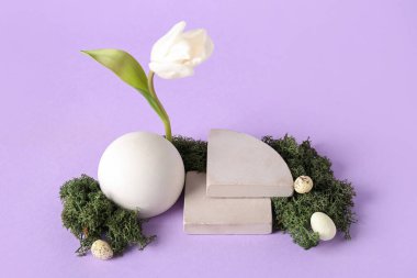 Composition with podiums, tulip flower, Easter eggs and moss on lilac background