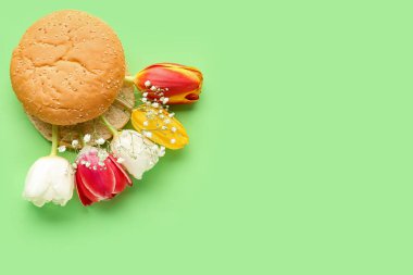 Creative composition with burger bun and beautiful flowers on green background