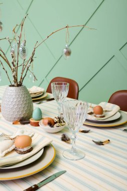 Festive dining table with eggs and pussy willow branches served for Easter celebration near green wall