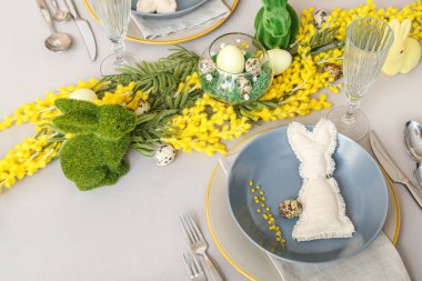Beautiful table setting with eggs, mimosa flowers and bunnies served for Easter celebration
