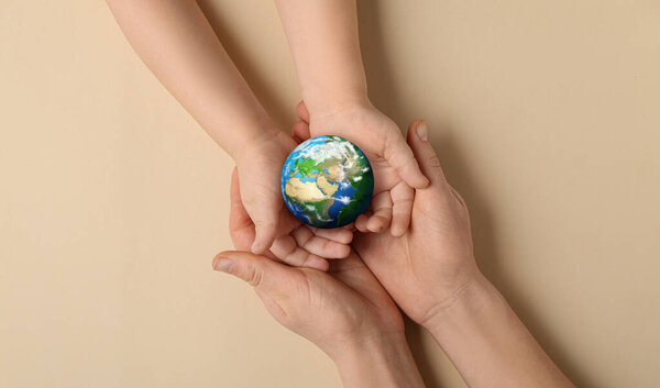 Hands of mother and child holding small planet Earth on beige background