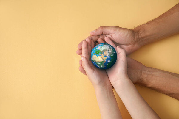 Hands of father and child holding small planet Earth on beige background