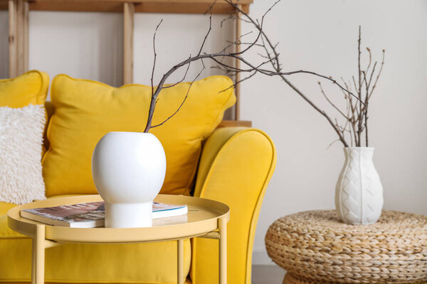 Vase with tree branches and magazine on table in living room, closeup