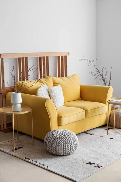Interior of living room with yellow sofa and tree branches in vase