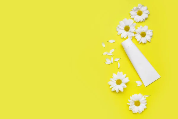 Composition with tube of cosmetic product and chamomile flowers on yellow background