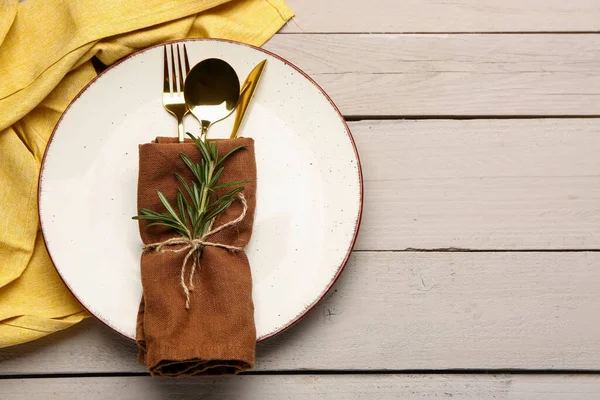 Plate with napkin, set of cutlery and rosemary on white wooden background